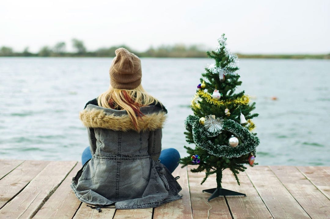 A young woman sitting on a dock with a Christmas tree.