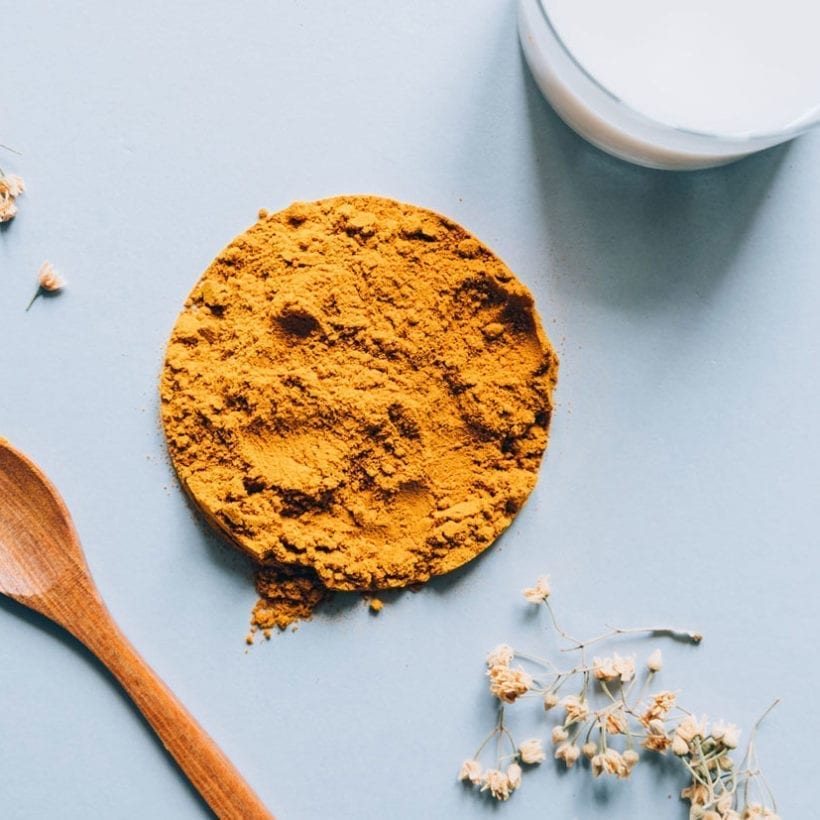 Overhead shot of turmeric powder and a wooden spoon on a light blue background.