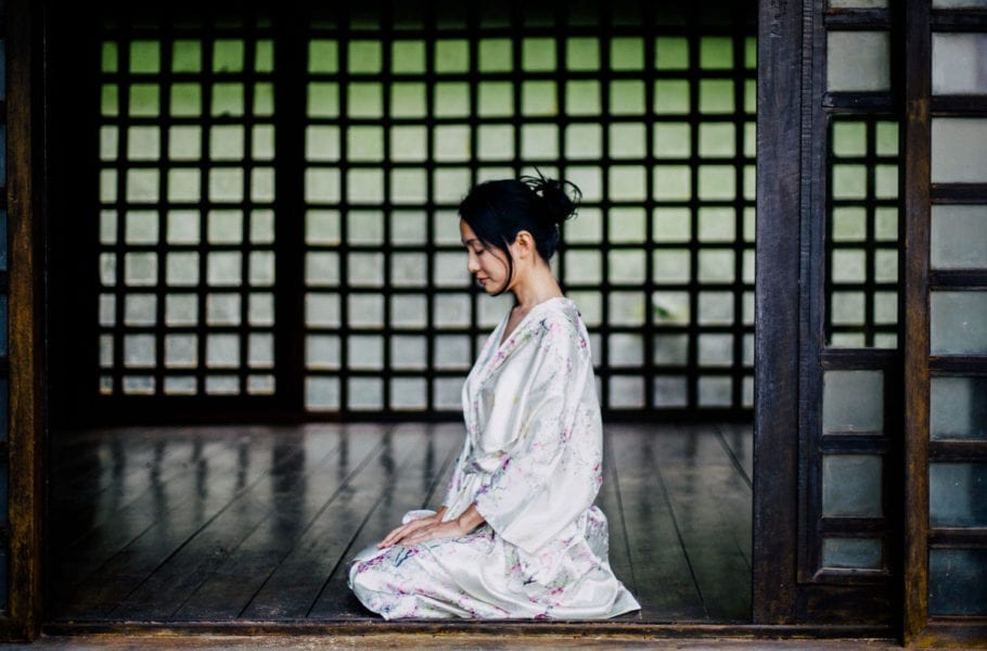 A Japanese woman in a silk kimono sits in a traditional Japanese house.