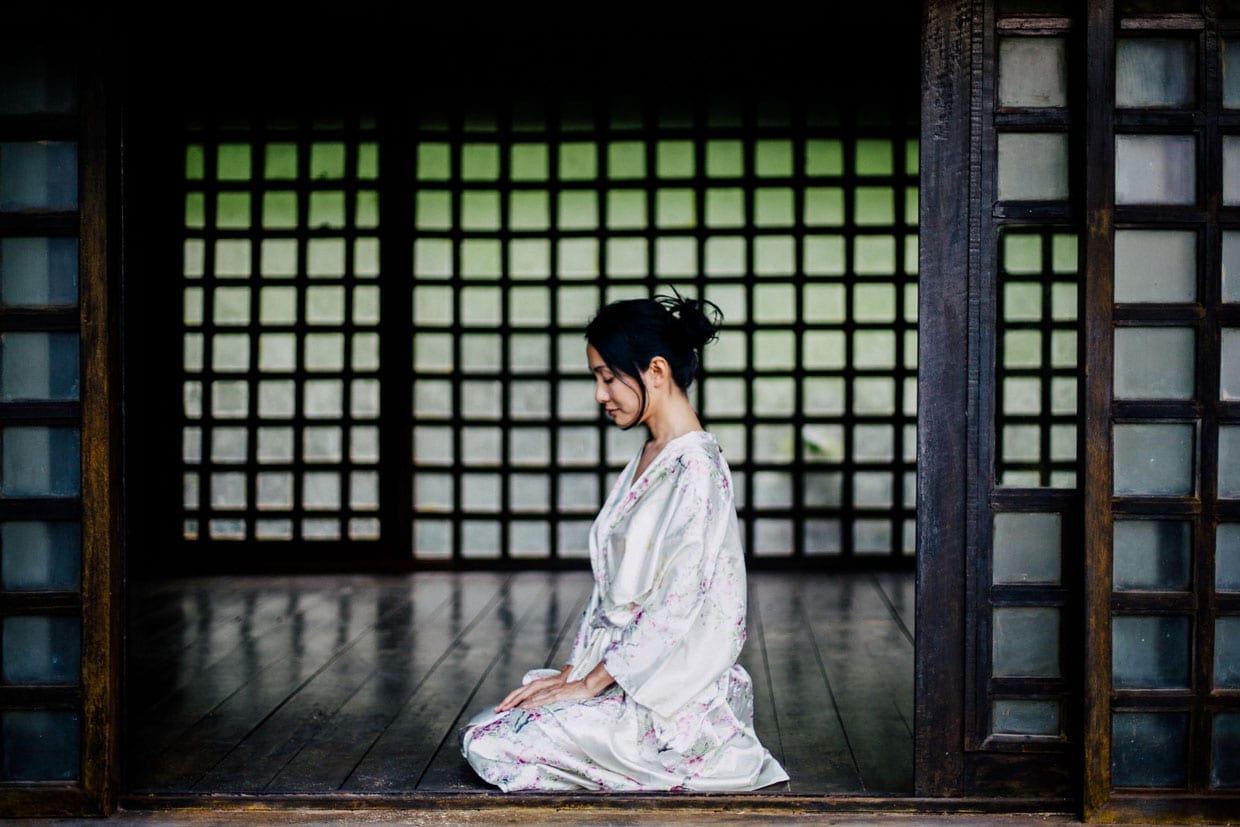 A Japanese woman in a silk kimono sits in a traditional Japanese house.