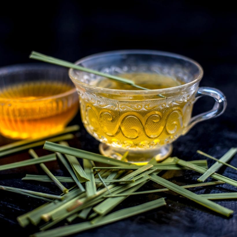 Close up of Iced lemon grass tea in a transparent cup on wooden surface with raw lemon grass around it.