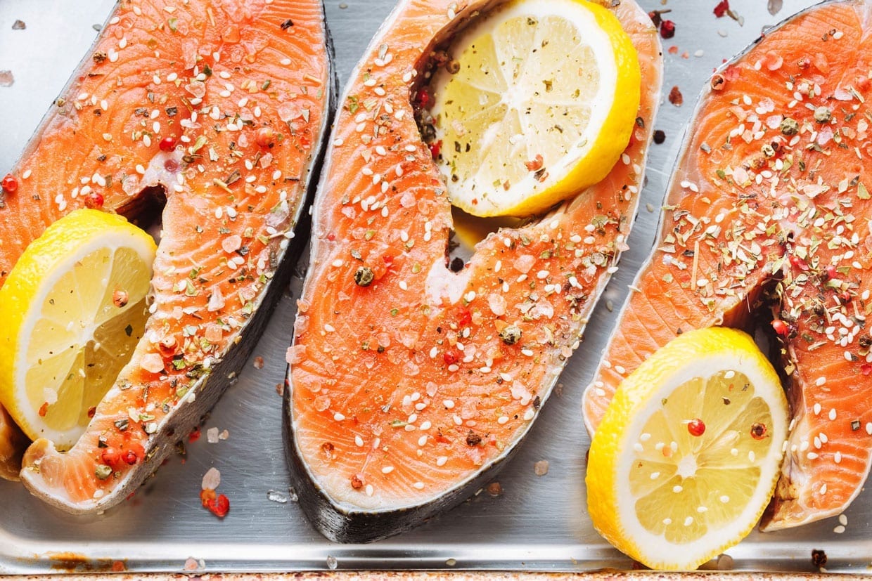 Raw fish steaks covered with salt with lemons on baker pan.