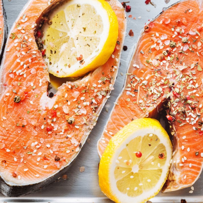 Raw fish steaks covered with salt with lemons on baker pan.