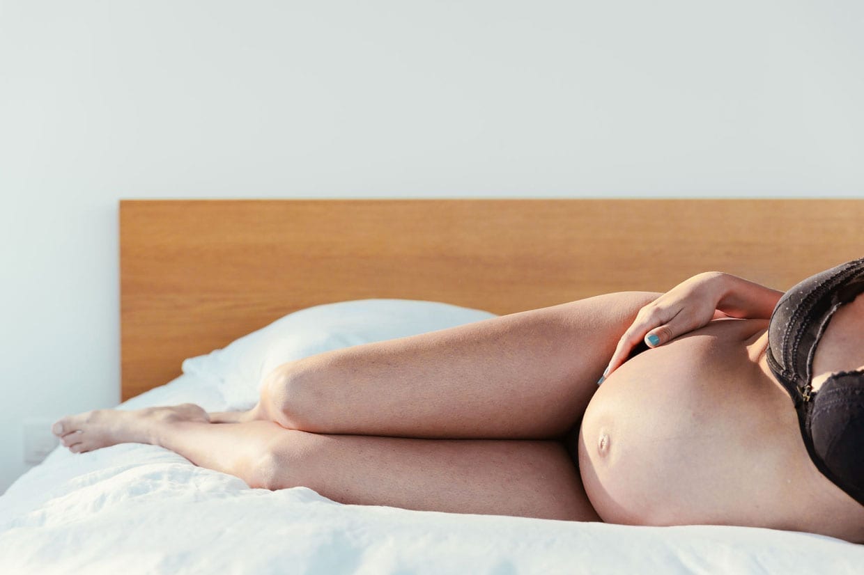 A pregnant woman in lingerie lies on a bed.