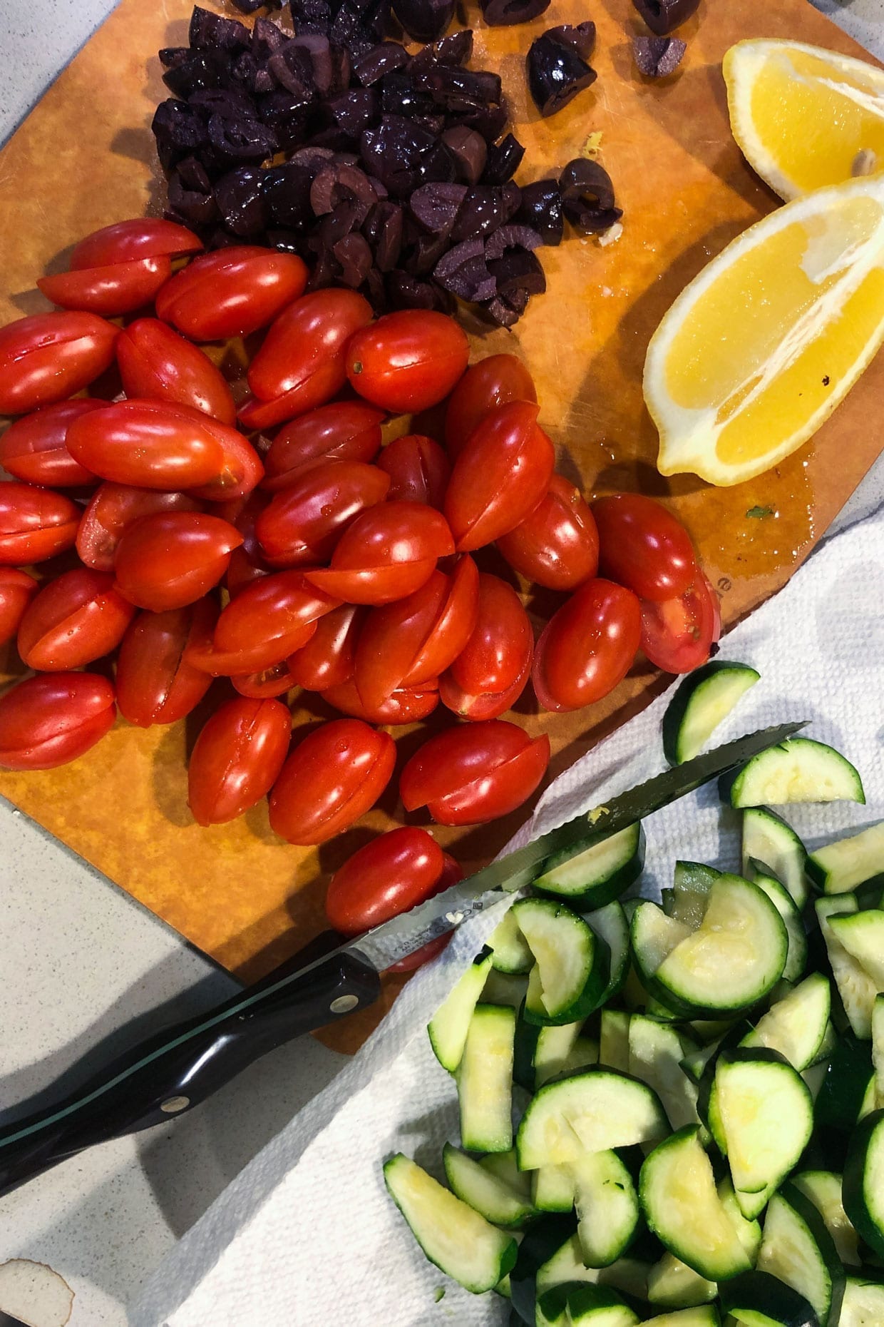 Overhead shot of cutting board, knife, tomatoes, zucchini, and a lemon.