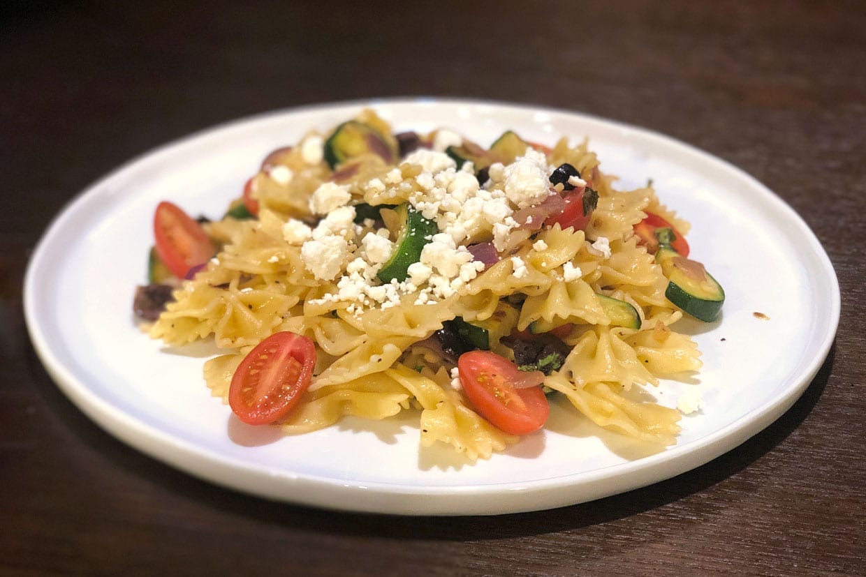 Farfalle with Zucchini, Tomatoes, Olives and Feta on a white plate.