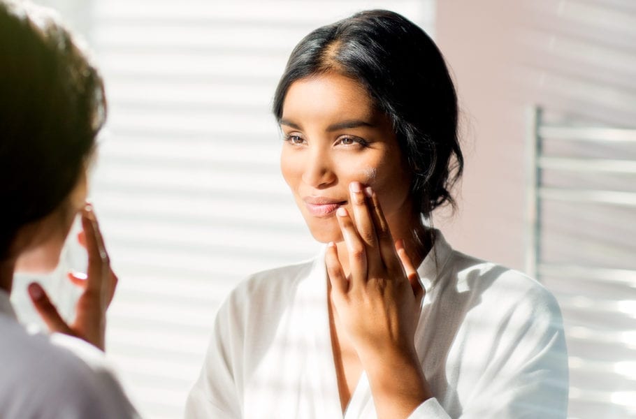 A woman applying skincare products in the bathroom mirror.