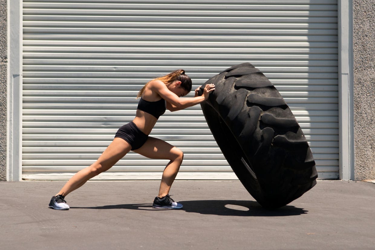 A woman pushing a giant tire.