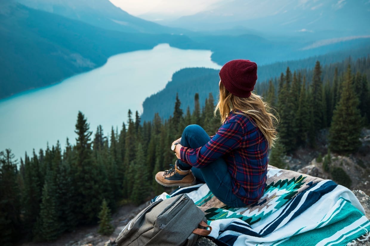 A young woman sitting on a blanket on the edge of a cliff overlooking Peyto Lake.