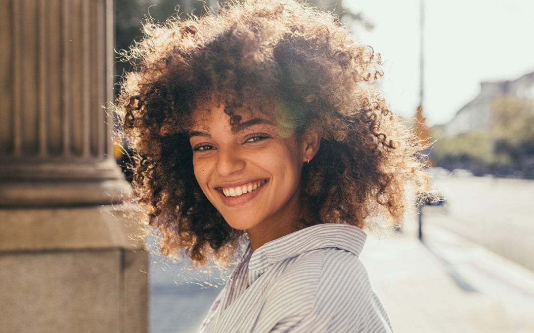 A mixed race woman with an afro smiling.