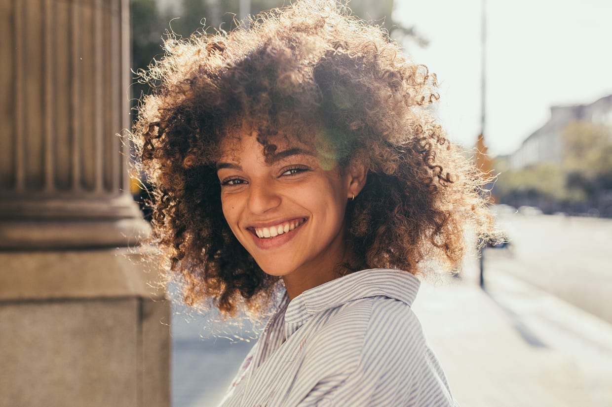 A mixed race woman with an afro smiling.