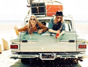 Two young women spraying soda from the back of a car.