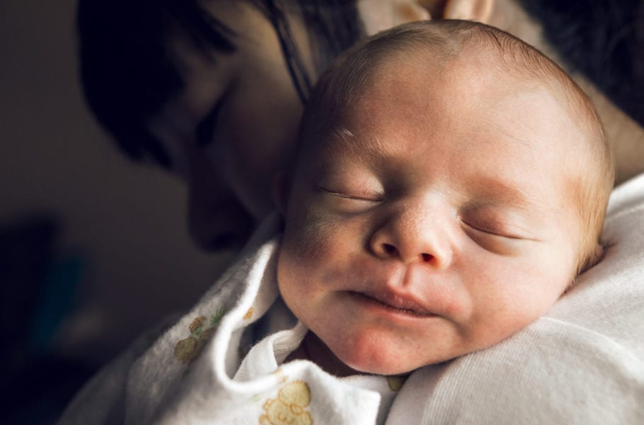 A 10-day old newborn boy soundly sleeping on his mother's shoulder.