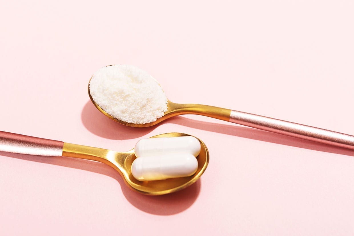 Powder and pills on golden spoons on a pink background.