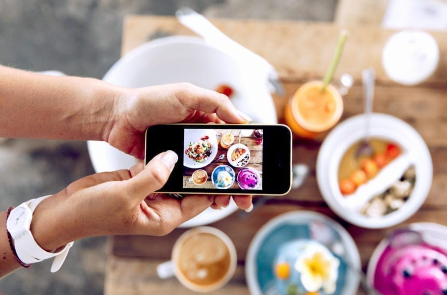 Close up of hand taking an overhead photo of food on a wooden table.