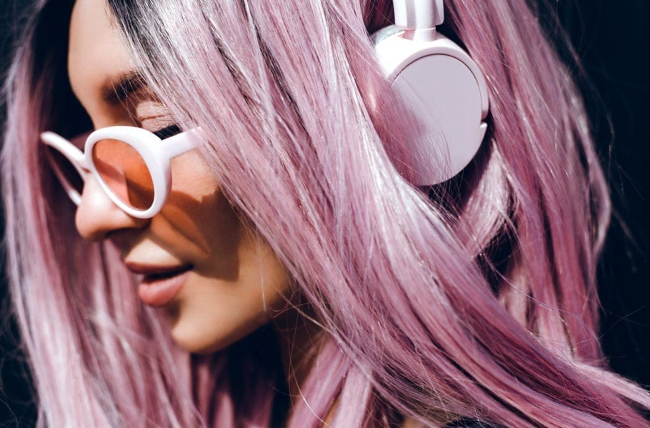 A woman with purple pink hair listening to podcasts on headphones.