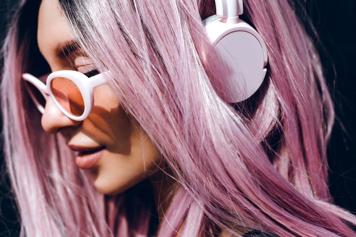 A woman with purple pink hair listening to podcasts on headphones.