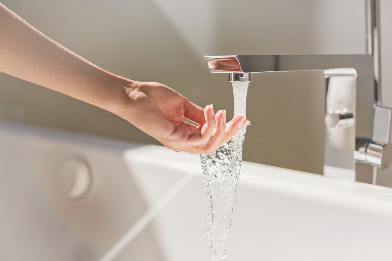 A woman's hand touches water from a faucet.