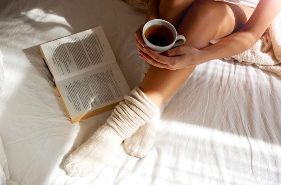 A woman wearing knitted socks holds a cup of tea in bed.