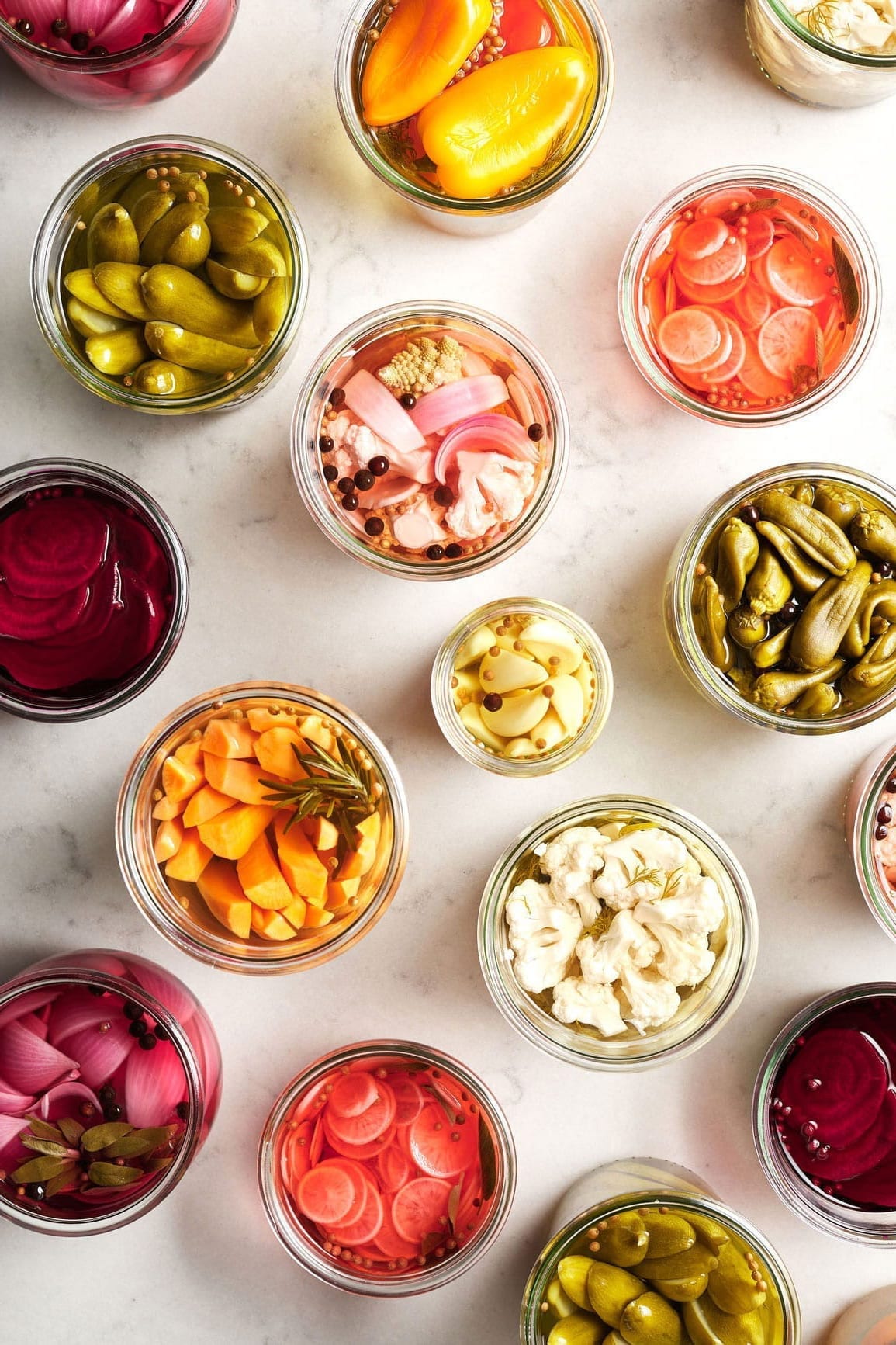 An overhead photo of pickled vegetables on a white marble background.