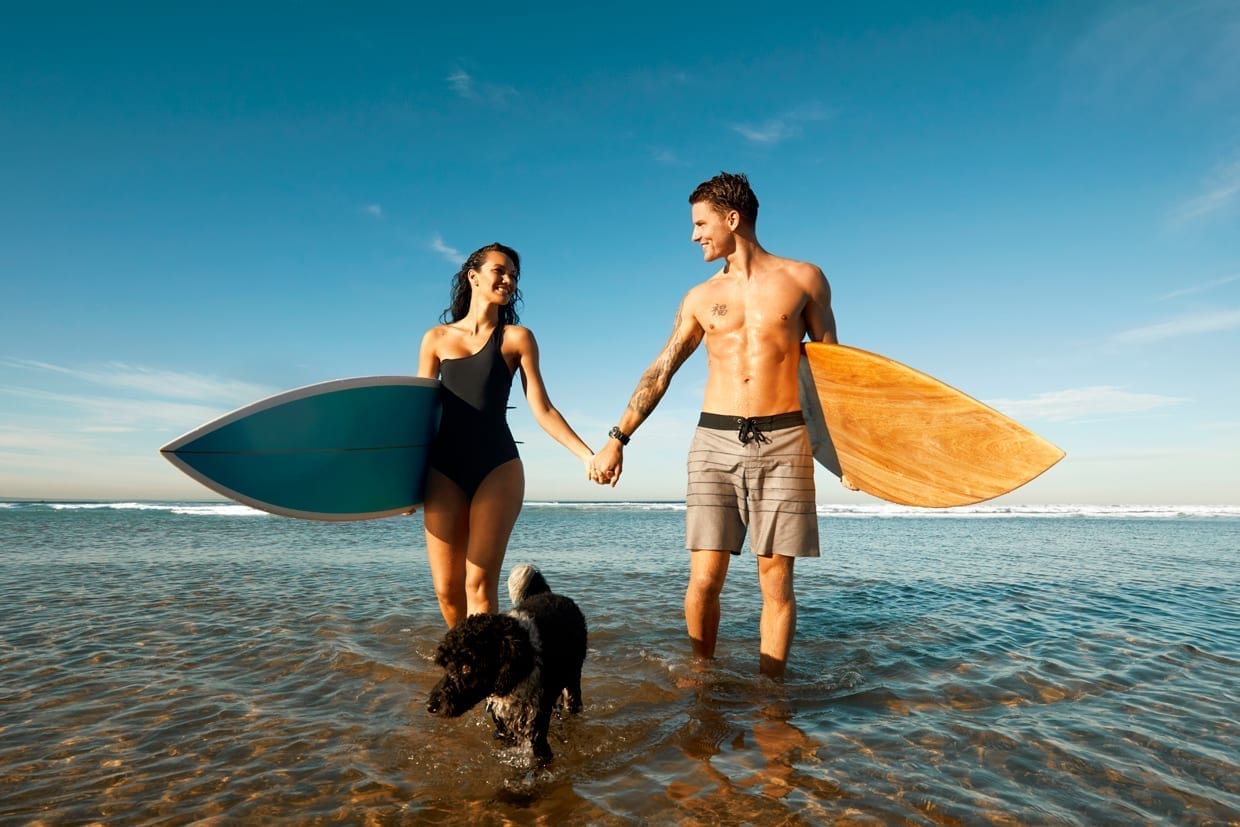 A couple with surfboards and their dog at the beach.