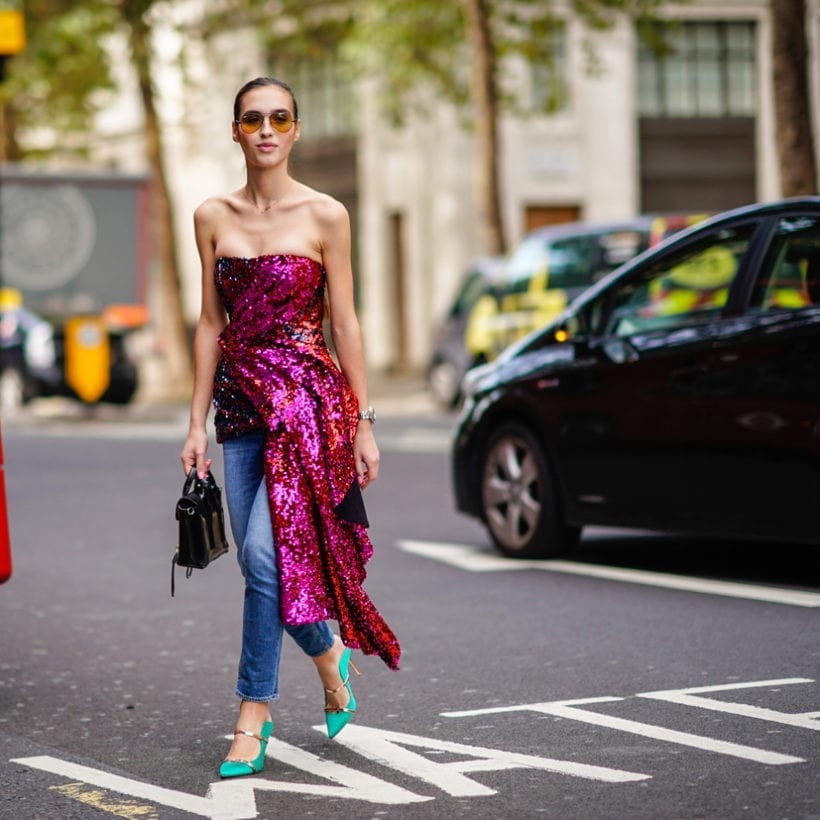 A woman in a purple glitter off-the-shoulder dress, blue denim jeans, green shoes, during London Fashion Week, Sept. 14, 2018.