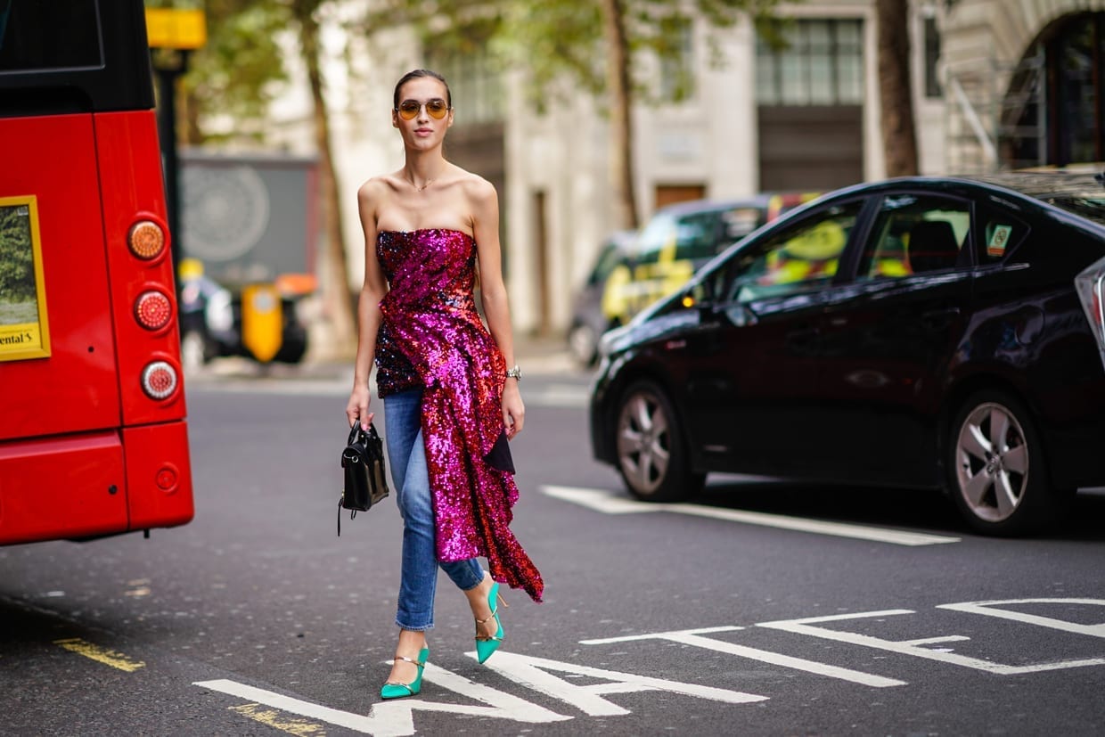 A woman in a purple glitter off-the-shoulder dress, blue denim jeans, green shoes, during London Fashion Week, Sept. 14, 2018.
