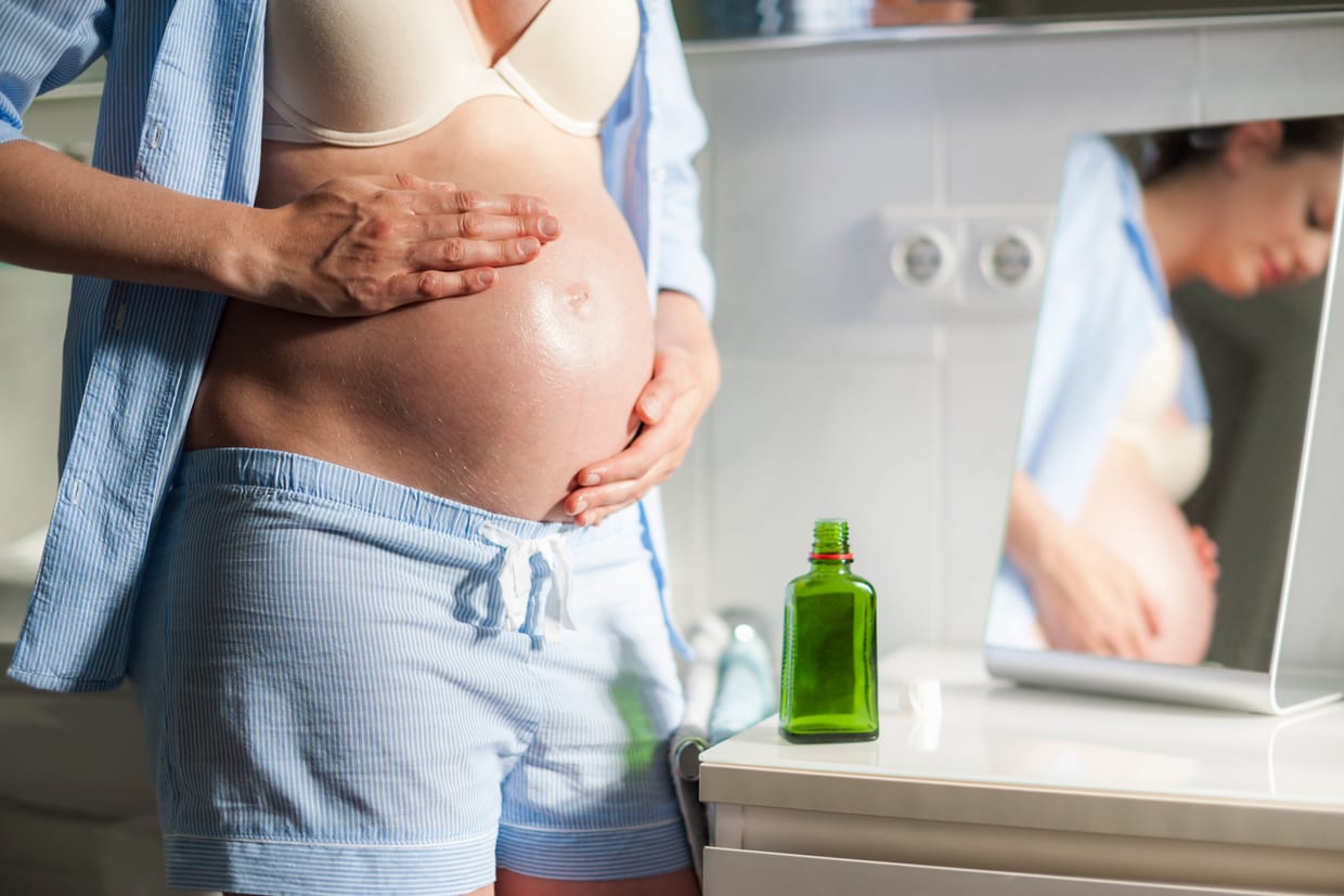 A pregnant woman applies an oil to her belly.