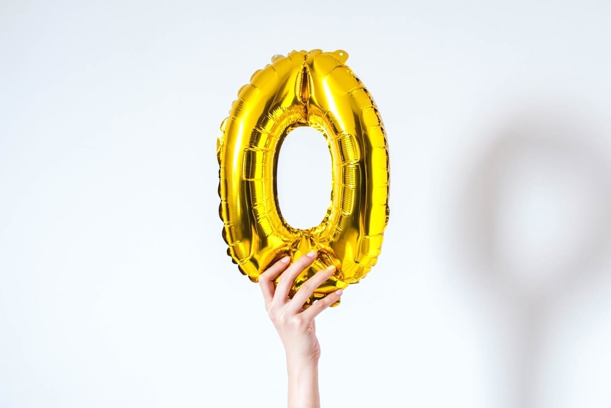 A young person is holding a golden-colored number zero on a white background.