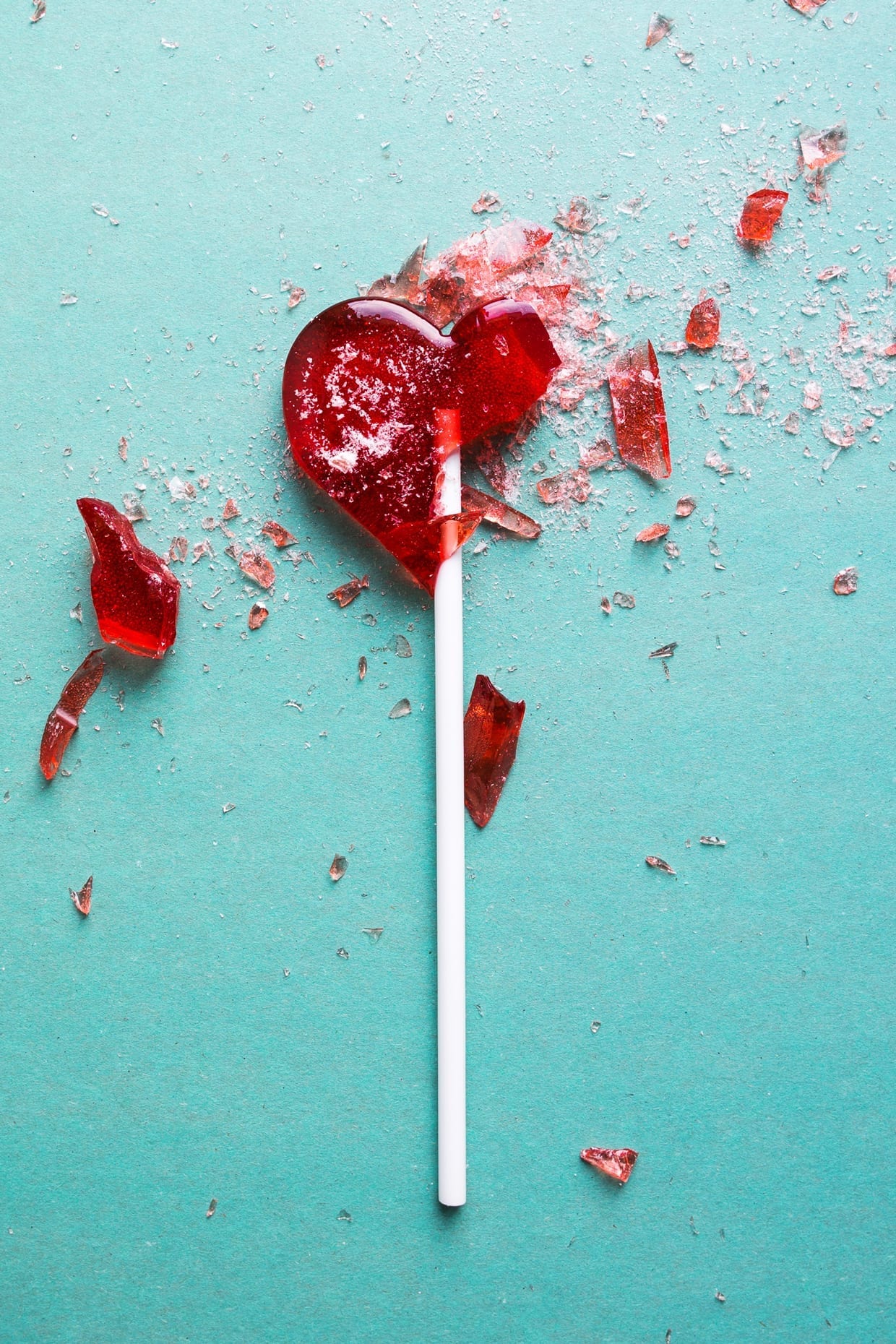 A shattered red heart shaped lollipop on a light blue background.
