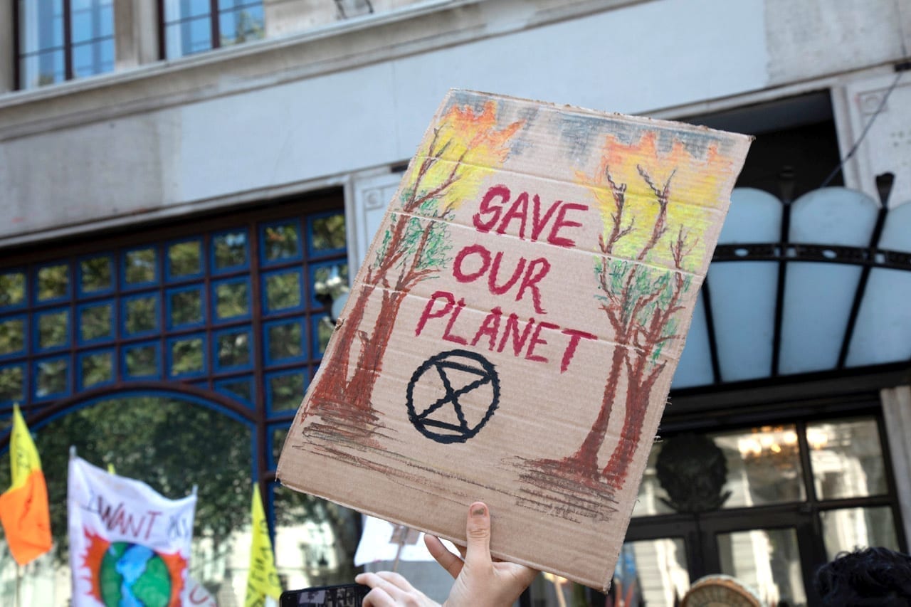 A hand holds up a cardboard sign reading, "Save Our Planet."