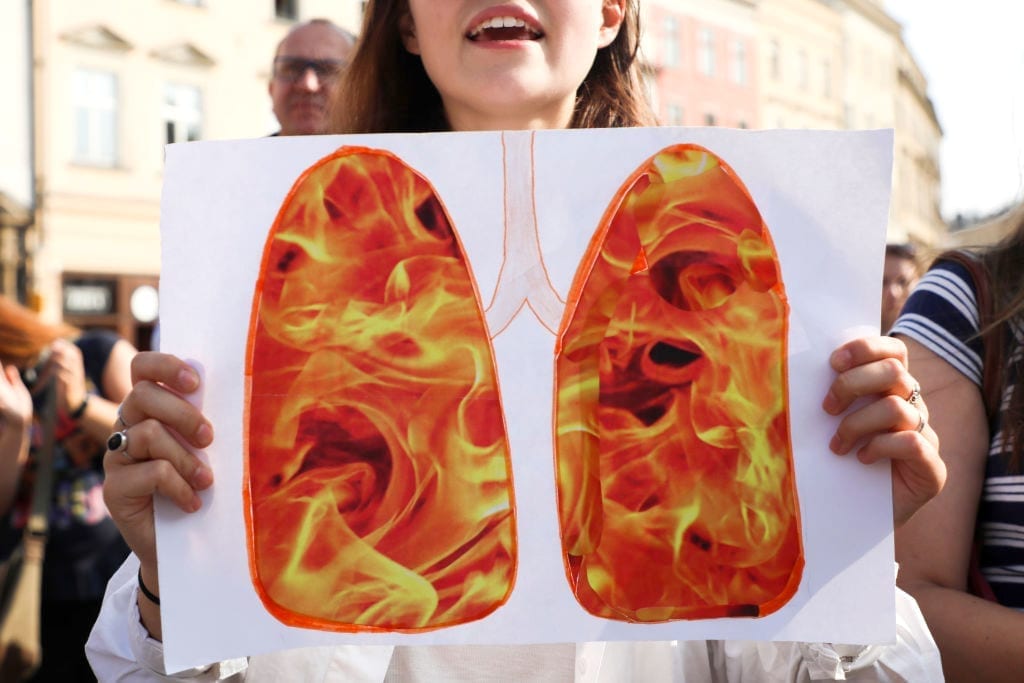 A woman holds up a paper with a photo of burning lungs.