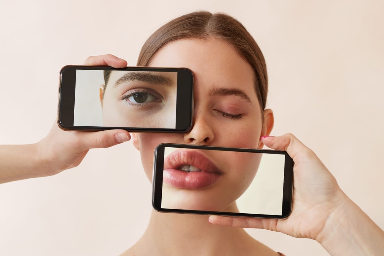 Conceptual shot of young woman's eye and lips being covered with exaggerated ones on smartphone screens.