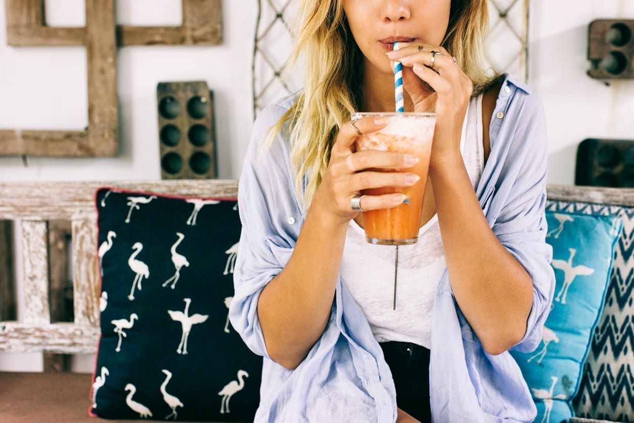 A girl holding a cup drinking through a paper striped straw.