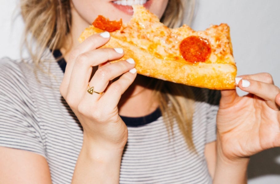 A woman eating a slice of pepperoni pizza.