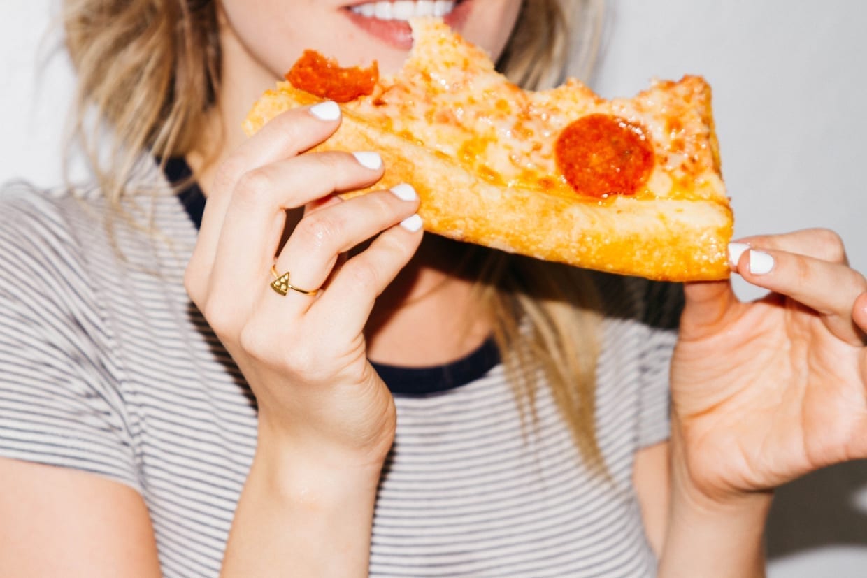 A woman eating a slice of pepperoni pizza.