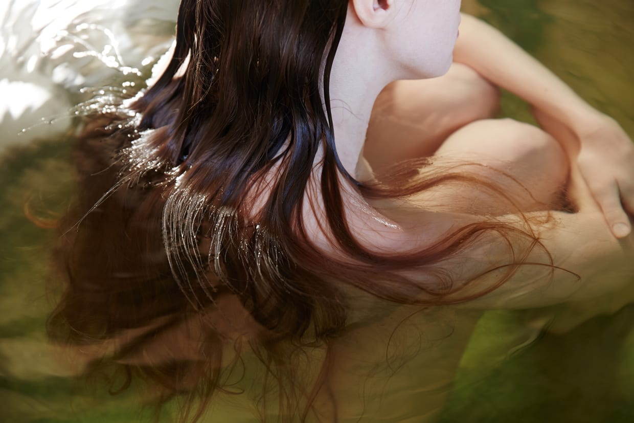 Midsection of redhead young woman relaxing in water at Japanese spa and hot springs.
