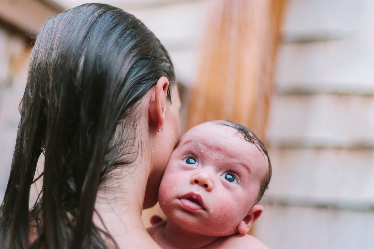 A woman and her newborn baby in an outdoor shower.