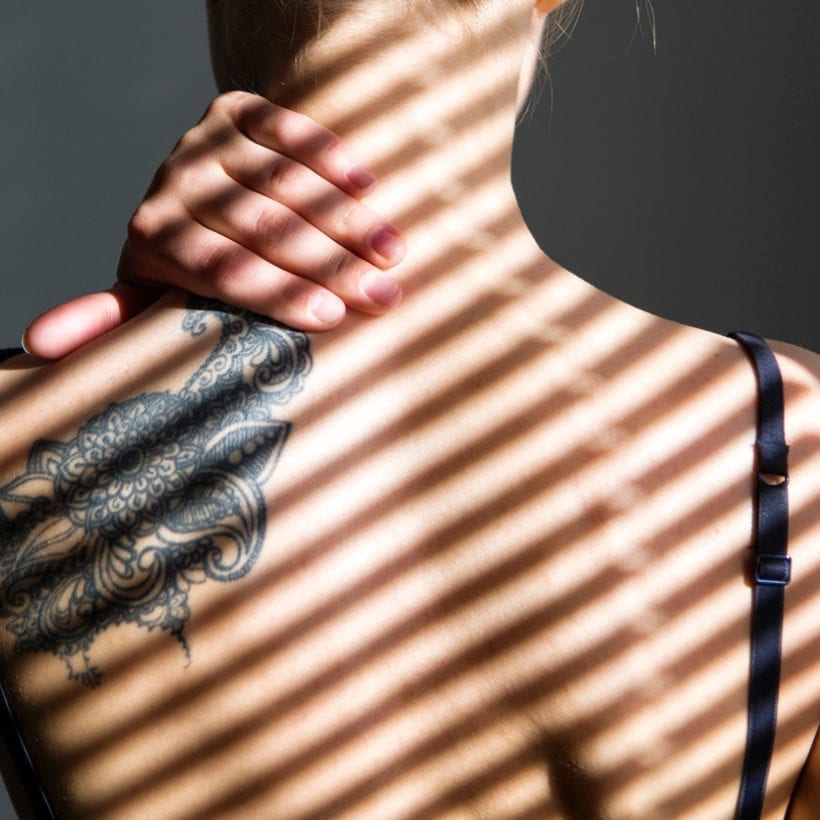 Back view of tattooed female back with shadow stripes on body.