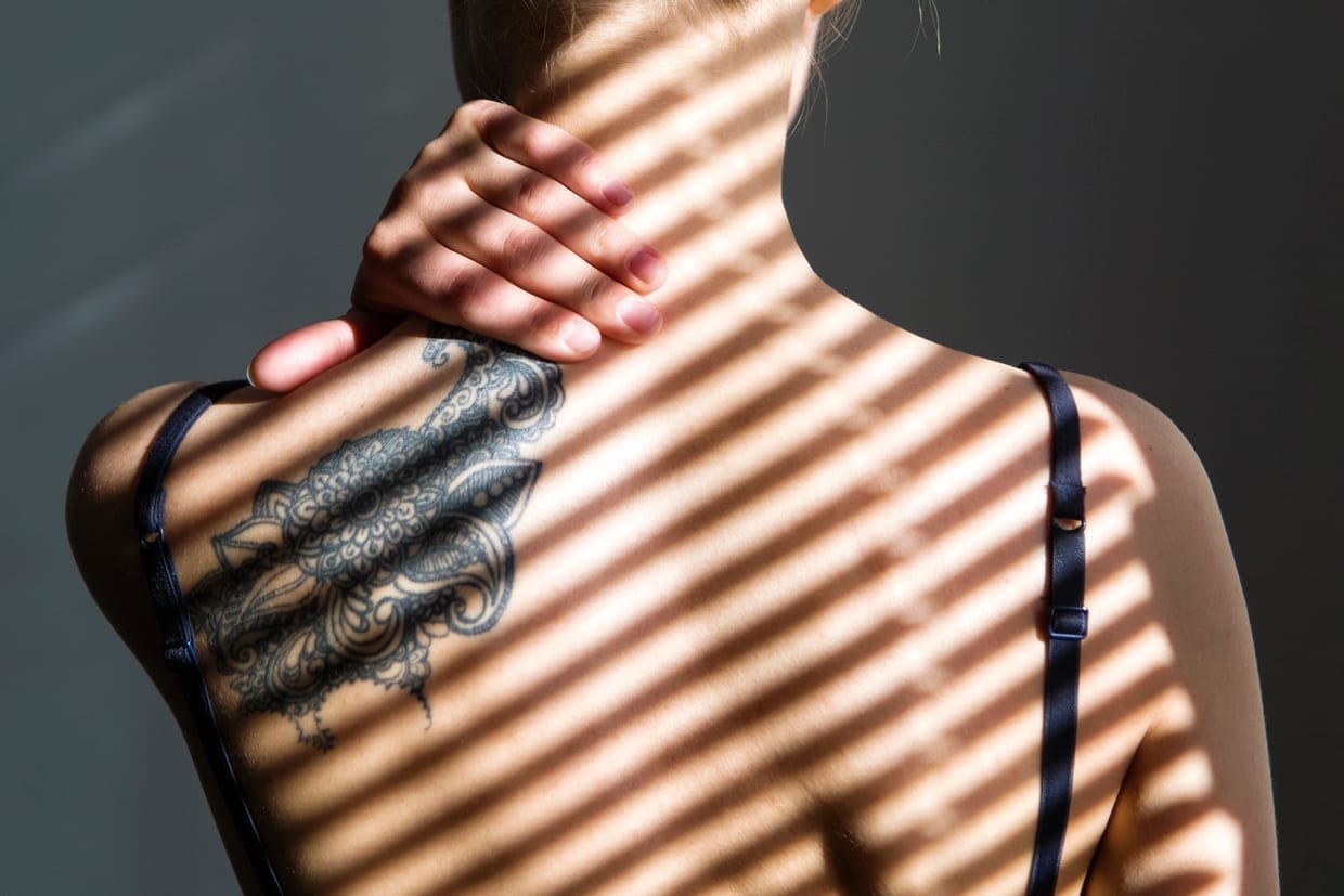Back view of tattooed female back with shadow stripes on body.