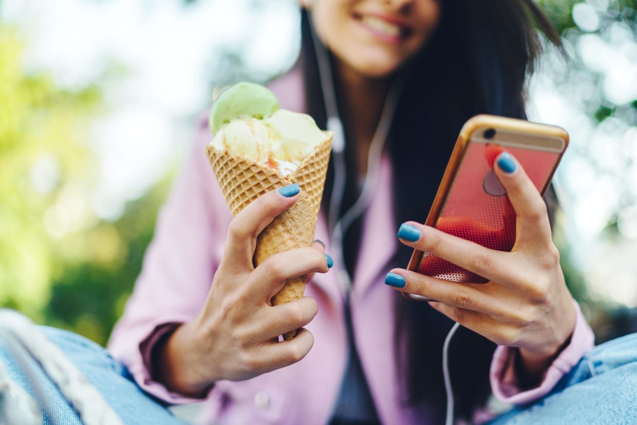 A woman looking at her phone and holding an ice cream cone.