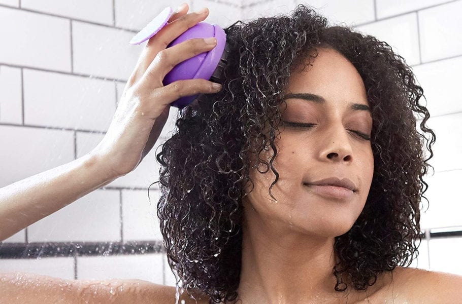 A woman using a brush in the shower.
