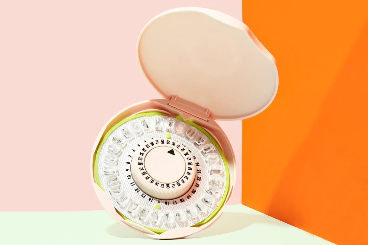 A birth control pill dispenser on a pink and orange background.