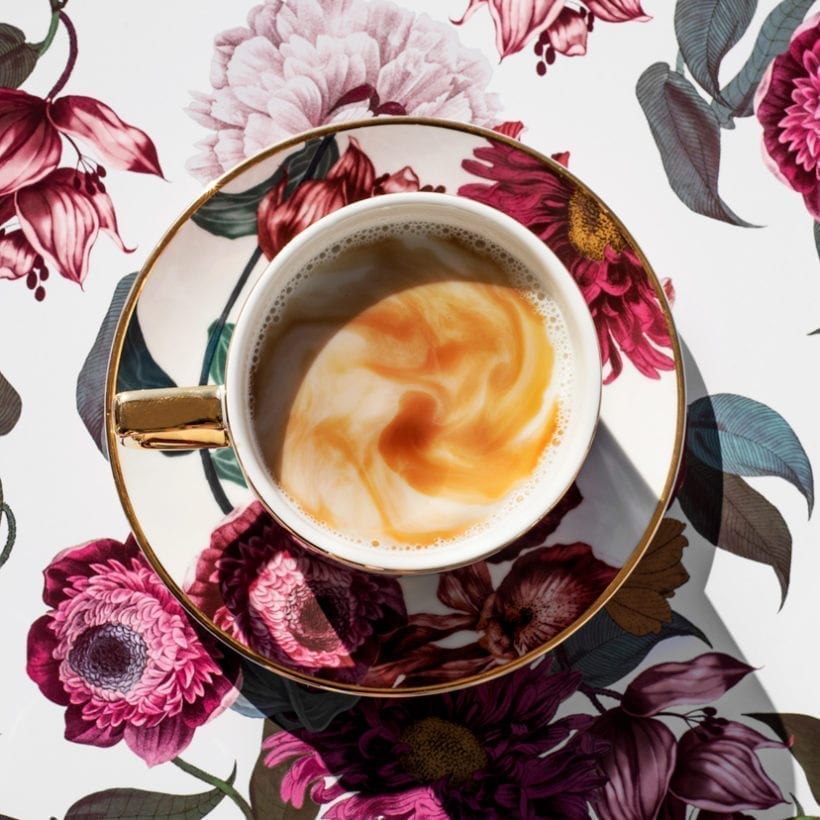 Flower-patterned cup filled with coffee on a flower-patterned background.