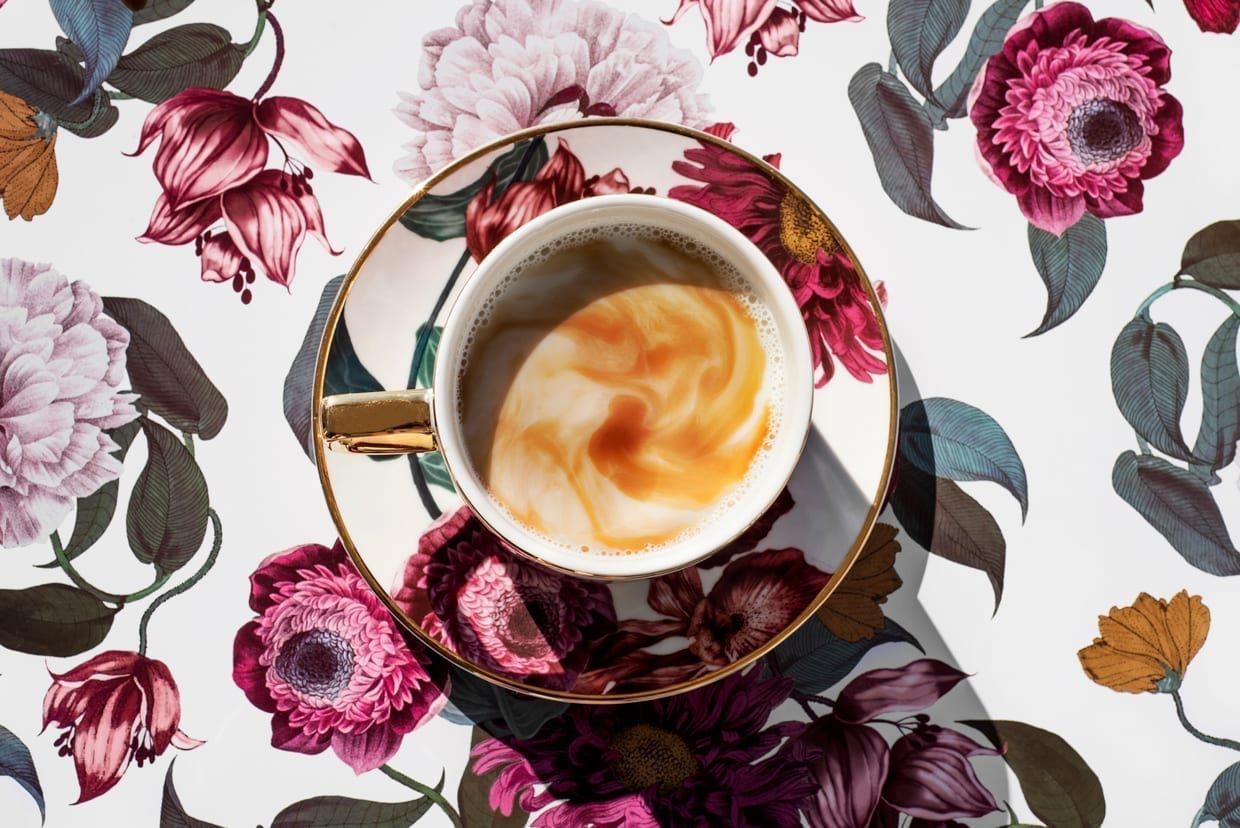 Flower-patterned cup filled with coffee on a flower-patterned background.