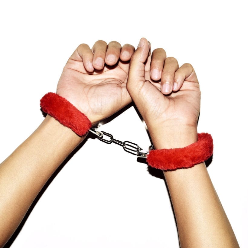 A pair of hands wearing red fluffy handcuffs.
