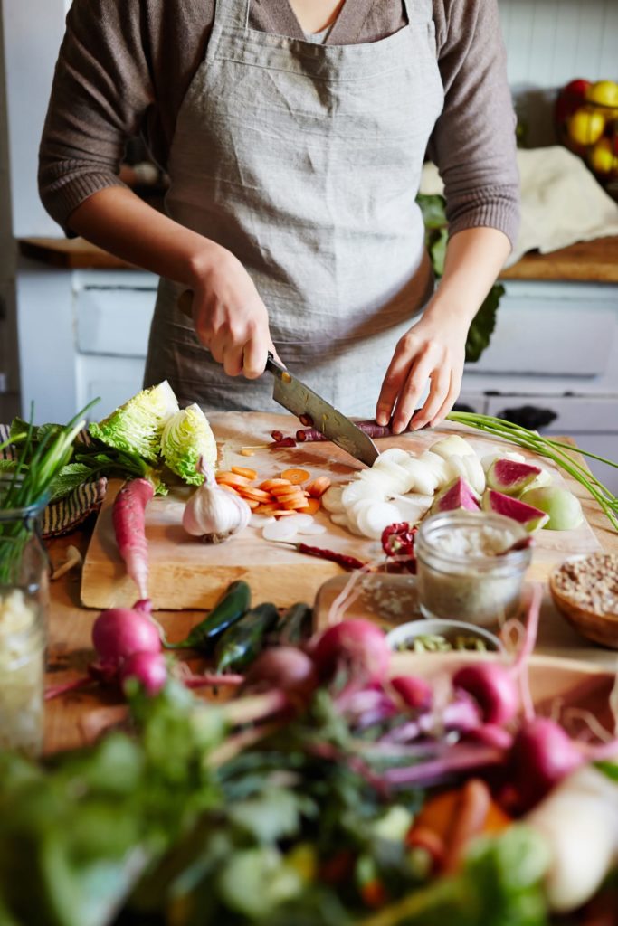 Woman wearing an apron slicing vegetables on a chopping board.