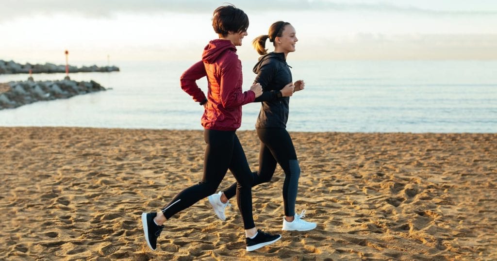 A mother and daughter running on the beach.