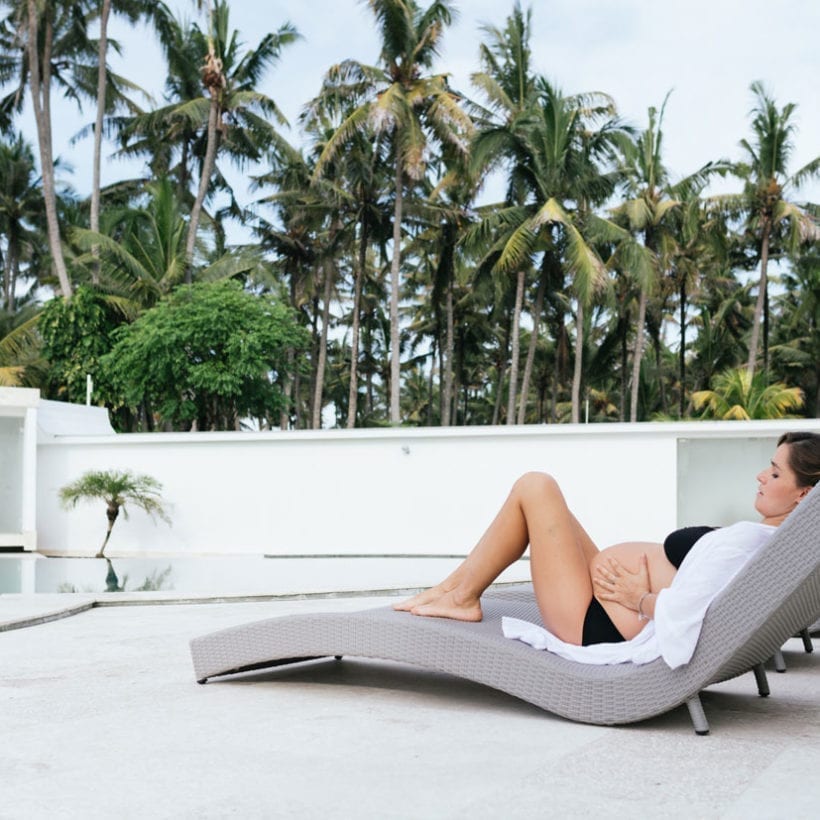 Pregnant woman relaxing at tropical villa outdoor by the swimming pool.