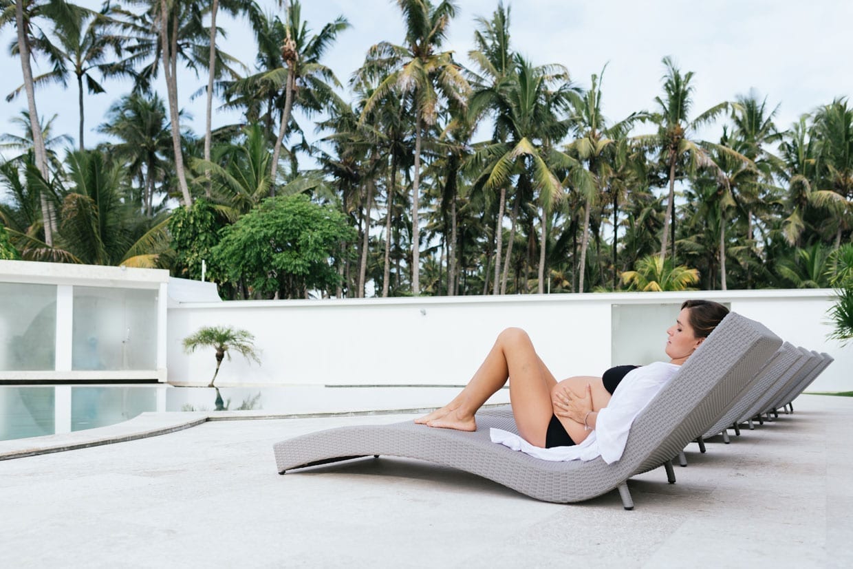 Pregnant woman relaxing at tropical villa outdoor by the swimming pool.